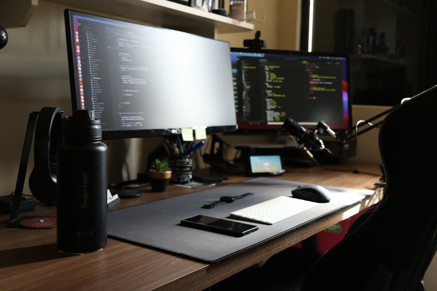 Two computer monitors displaying code on a dark wood desk.
