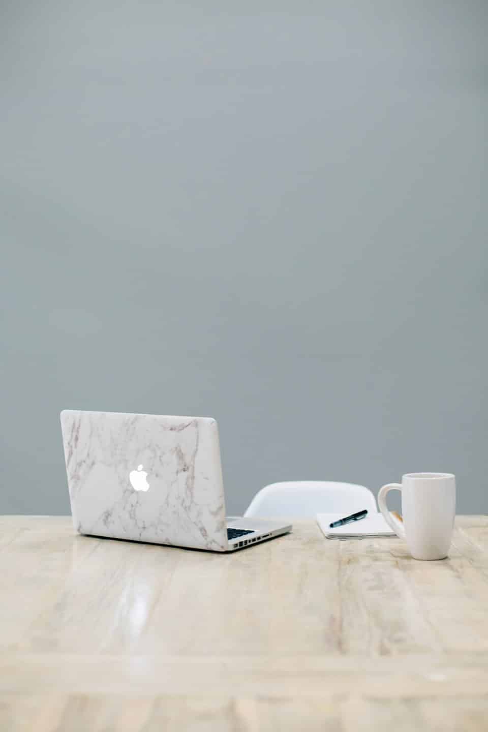 Laptop, notebook, and coffee mug on a wooden desk.