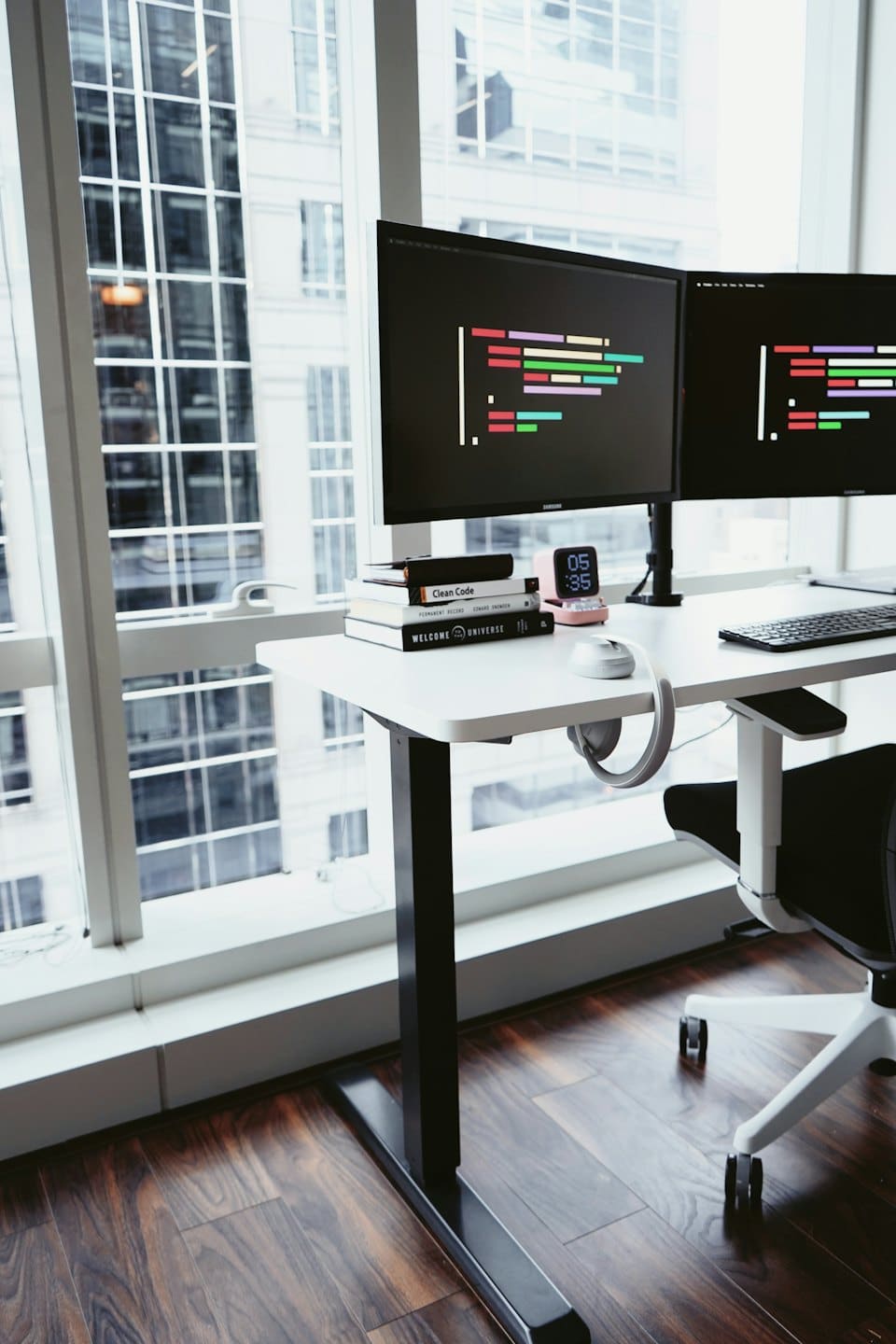 Standing desk with computers and books by a city window.